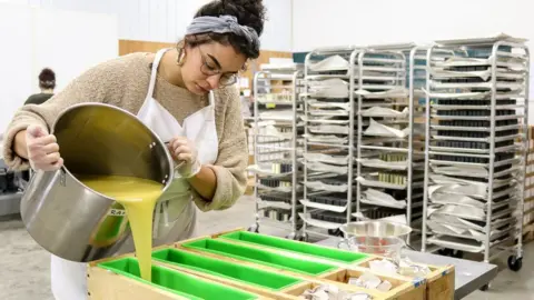 A Meow Meow Tweet staff member pours a soap mixture into moulds