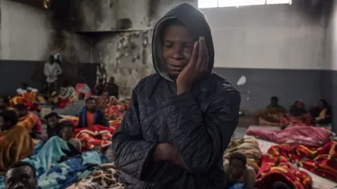 AFP A migrant holds his head as he stands in a packed room at the Tariq Al-Matar detention centre on the outskirts of the Libyan capital Tripoli on November 27, 2017