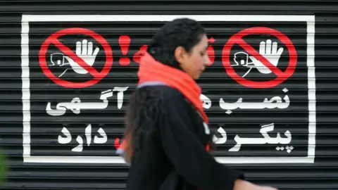 ABEDIN TAHERKENAREH/EPA An Iranian woman walks next to a closed shop without wearing a headscarf, in Tehran, Iran, 10 August 2023