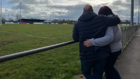 Ben and Amy Branson embracing each on the rugby club field