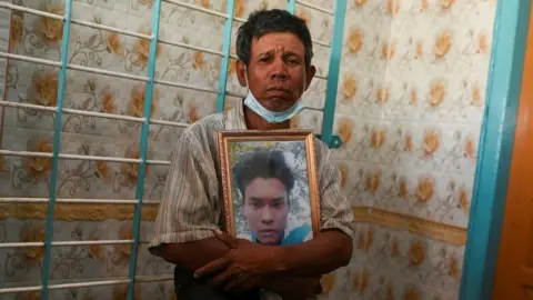 Reuters A man holds a picture of one of a victim who was shot dead during the anti-coup protest, in a cemetery at the outskirts of Yangon, Myanmar, March 5, 2021. REUTERS/Stringer