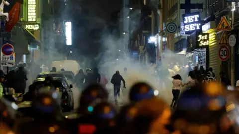 Getty Images Rioters run as French police officers use tear gas in Paris on 2 July