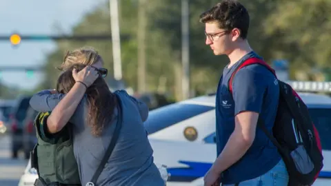 EPA Woman comforted by police officer outside Marjory Stoneman Douglas High School in Parkland, Florida, on 14 February 2018