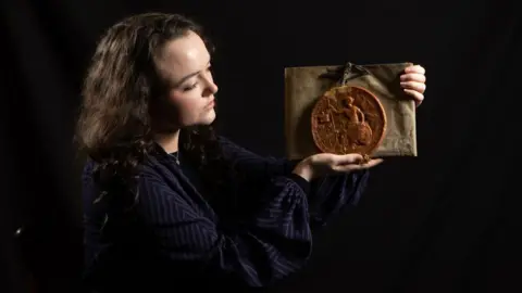 Duncan Lomax A woman holds an artefact in her hands