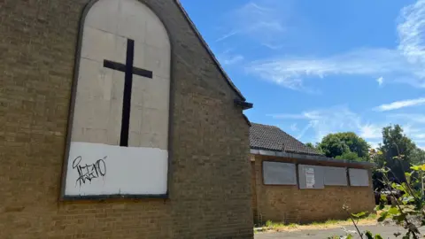 Kris Holland/BBC A modern brick-built church, with windows boarded up and graffiti showing