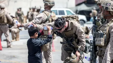 Reuters A US Marine and a child spray water at each other during an evacuation at Hamid Karzai International Airport, Kabul, Afghanistan, 21 August 2021