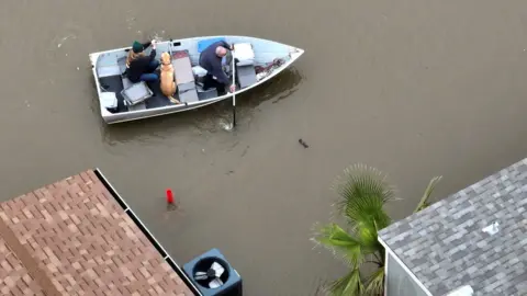 Reuters A man rows a boat with a woman and a dog in floodwater