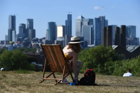 Kirsty O'Connor / PA A woman sunbathes on a deck chair in Greenwich Park, with buildings in the distanc
