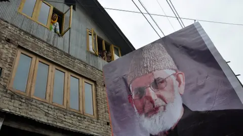 Getty Images Kashmiri Muslim women look from the windows of there house as a poster of senior separatist leader Syed Ali Shah Geelani is carried by the people during a pro freedom demonstration in Srinagar.