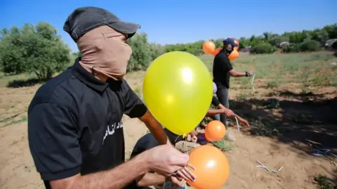 Getty Images Masked Palestinians launch incendiary balloons from the Gaza Strip towards Israel (15 June 2021)