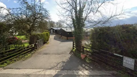 Google Entrance to farm with low fences either side and trees.