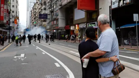 Reuters A couple hugs each other as police fire tear gas into the crowds to disperse anti-national security law protesters during a march at the anniversary of Hong Kong"s handover to China from Britain in Hong Kong, China