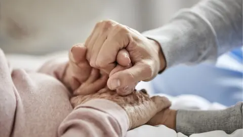 Getty Images Carer holding hands with elderly person