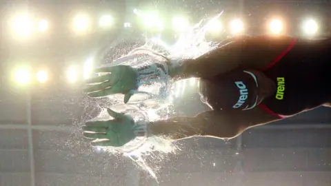Reuters A swimmer is seen from underneath. The arena lights are clearly visible through the clear water.