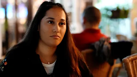 Sharon - a young woman sitting in a restaurant/bar