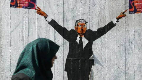 Getty Images A Muslim woman walks past a street artist's rendition of U.S. President Donald Trump on 27 June, 2017 in Berlin, Germany