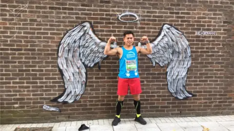 BBC Neil Calucag standing in front of a pair of painted angel wings