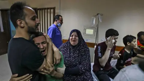 Getty Images A member of the Abu Dayer family, surrounded by relatives, cries at the Al-Shifa hospital after the death of his father and cousin in an Israeli air strike