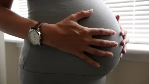 PA Media Woman holds her pregnant belly
