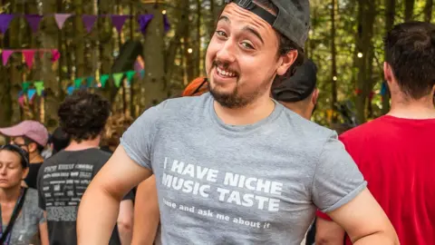 Dan Hess A man wearing a t-shirt that says "I have niche music taste come and ask me about it"