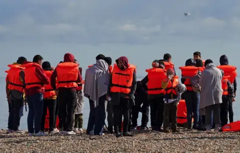 PA Media A group of people thought to be migrants on the beach in Dungeness, Kent, after being rescued in the Channel by the RNLI following following a small boat incident