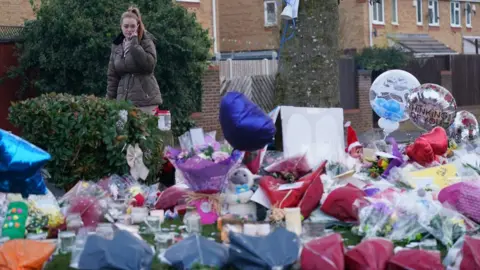 PA Media A woman lays flowers among the tributes near to Babbs Mill Park in Kingshurst, Solihull, after the deaths of three boys aged eight, 10 and 11 who fell through ice into a lake in the West Midlands.