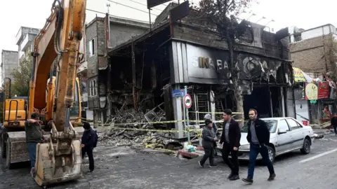 Reuters File photo showing people walking past a burned bank in Tehran, Iran (20 November 2019)