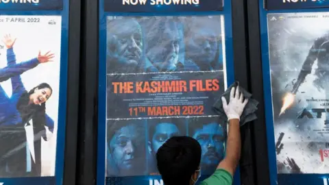 Getty Images In this picture taken on April 7, 2022, a worker cleans a display with the poster of the Bollywood movie 'The Kashmir Files', outside a cinema hall in New Delhi.