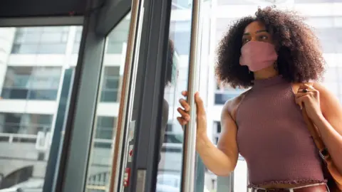 Getty Images Young woman entering office wearing face mask