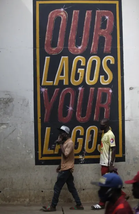 EPA Men wearing face masks walk past a mural reading "Our Lagos, Your Lagos".