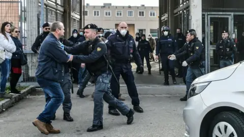AFP/Getty Images A man is restrained by a police officer outside a prison in Modena, Italy. Photo: 9 March 2020
