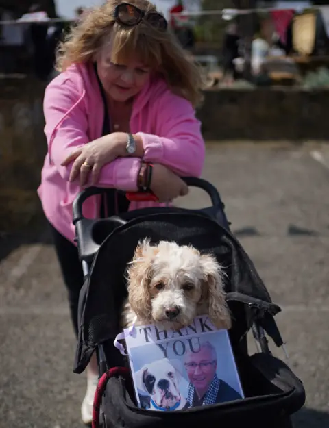 PA Media A person waits outside the Walnut Tree Pub with a dog in a pram and a picture of Paul O'Grady with the words "Thank you"