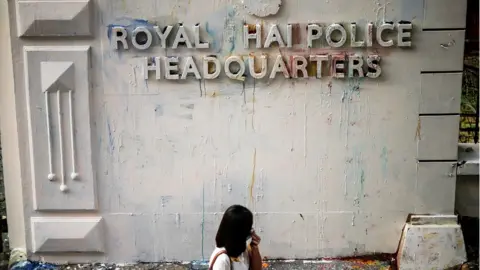 Reuters A woman reacts while walking past the damaged signage of the police headquarters