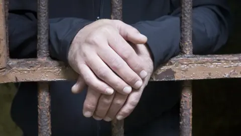 Getty Images Man's hands behind jail bars