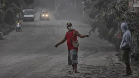 Getty Images Residents walk along a road covered in volcanic ash from Taal Volcano's eruption on January 13, 2020 in Lemery, Batangas province, Philippines