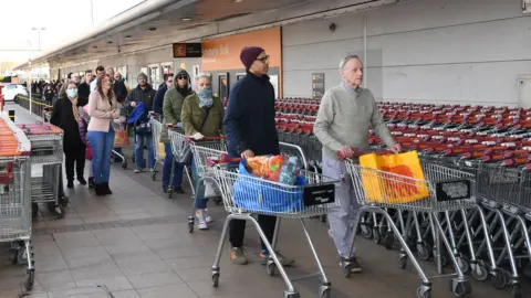 EPA Shoppers queue outside a supermarket in south London, Britain, 22 March 2020. Pensioners and vulnerable people has been struggling to buy their essential shopping due to unprecedented demand of Britons flocking to the supermarkets and panic buying due to the spread of the Coronavirus.