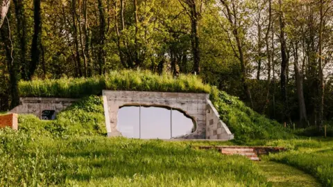 Will Scott / Corstorphine & Wright  A refurbished concrete bunker covered in grass with a glazed blast opening