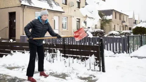 Jane Barlow/PA Wire Kasia Wojcik clears snow from her driveway in Penicuik, Midlothian