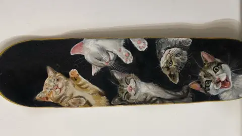 Ruby Parker A skateboard painted with several cats with happy facial expressions