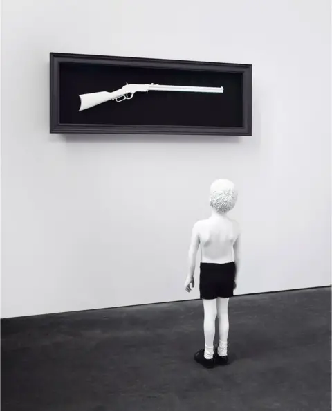 Maria Jose Jove Fundacion One Day (2015) is a monchrome sculpture in which a boy looks up at a rifle mounted on the wall