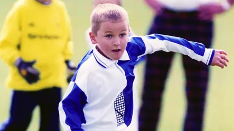 Pictures from Harry Kane Harry Kane is seen playing for Ridgeway Rovers as a child. The archive image shows him in his blue and white kit while people watch on behind him.