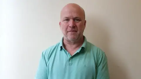 Carey Baxter, a man with shaved head, wearing a green polo shirt.