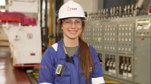 Piers Hopkirk/BBC Chloe Tilly - a woman in a blue work suit with a white hard hat.