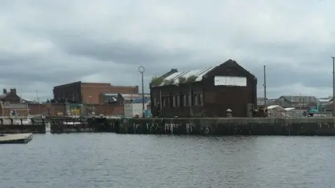 Christine Johnstone Clarence Graving Dock. A large basin of water with buildings next to it and high walls.