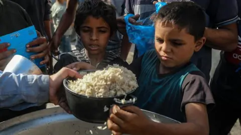 Two Palestinian boys receive a bowl of rice