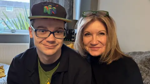 Sam Matthews and her son Charlie facing the camera. Charlie wears a cap with Nintendo on it and Sam has glasses on her head