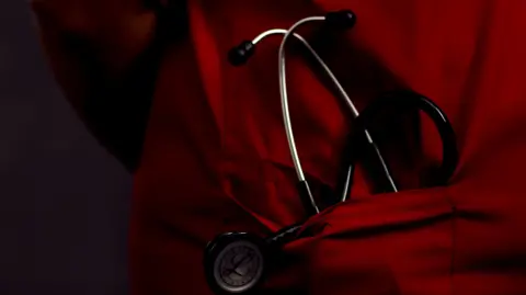 A stock photo of a medical professional in a red uniform and a stethoscope in their pocket. 