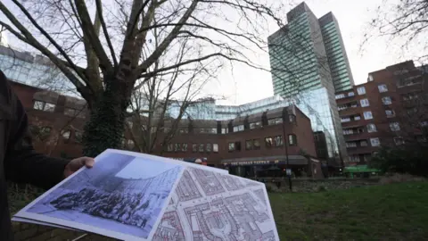 A woman's hand is just visible holding an old photo and map in which a tower block can be seen in the distance