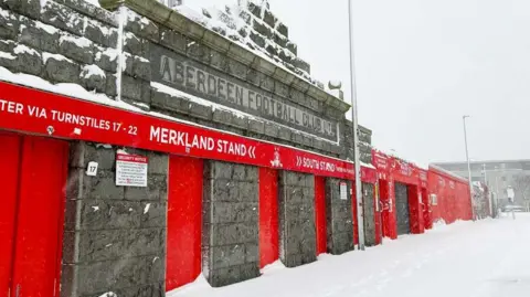 Aberdeen FC Aberdeen Football Club entrance covered in snow with red doors and signage.