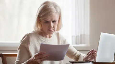 Serious frustrated middle aged senior woman worried reading bad news in paper letter document